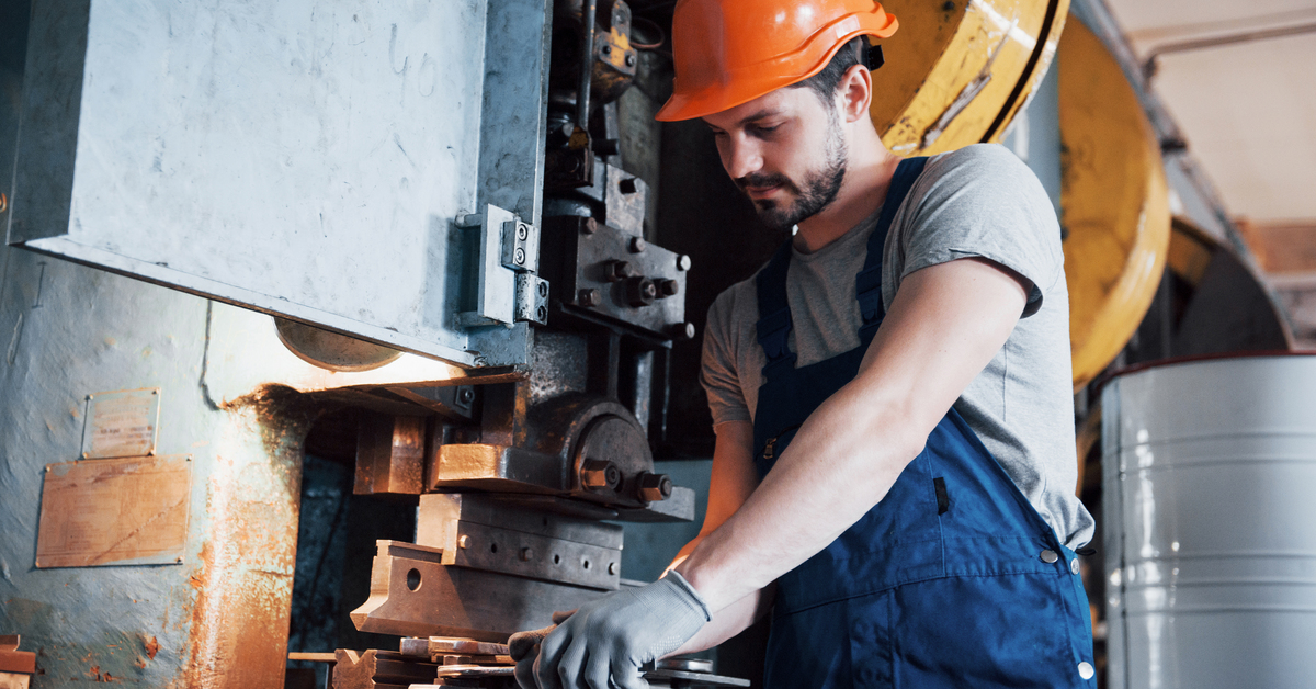 Portrait of a young worker in a hard hat at a large metalworking plant. The engineer serves the machines and manufactures parts for gas equipment.