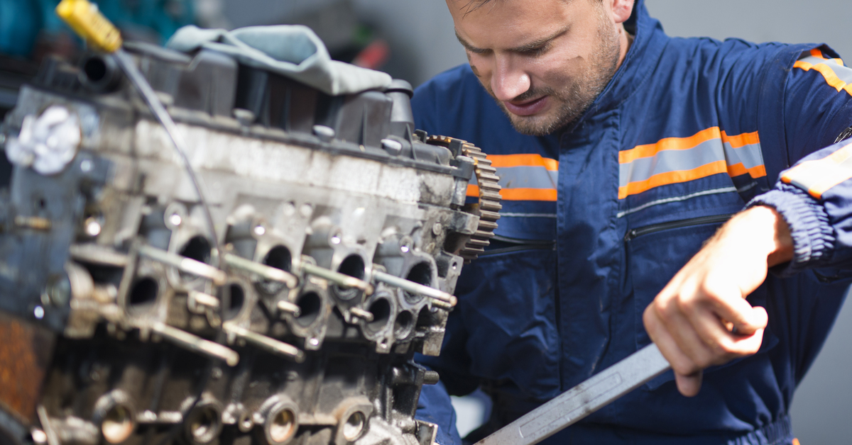 Professional car mechanic repairing automobile engine using wrench in work shop.